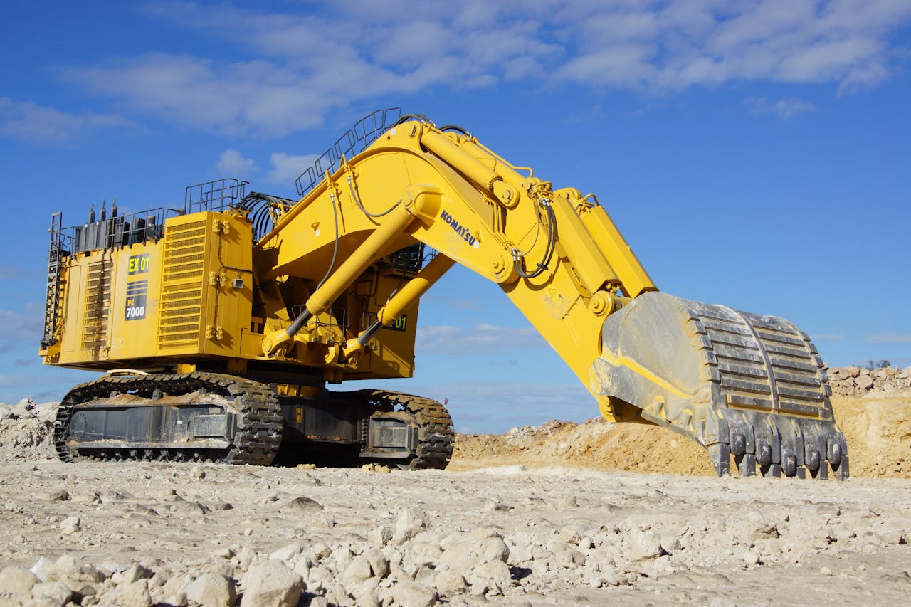 Yellow excavator in a sunny, open construction site, under a blue sky.